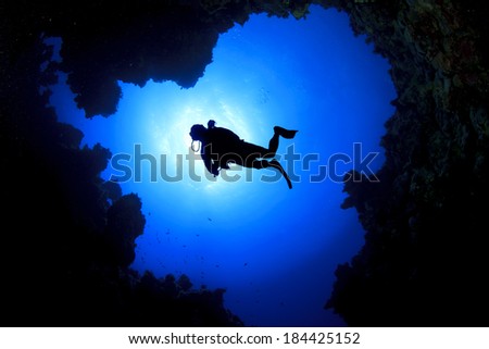 Scuba Diver swims over underwater cave, silhouette against sun
