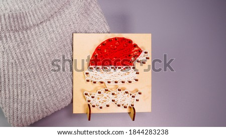 String art Santa Claus hat on a wooden frame with warm gray knitted sweater.