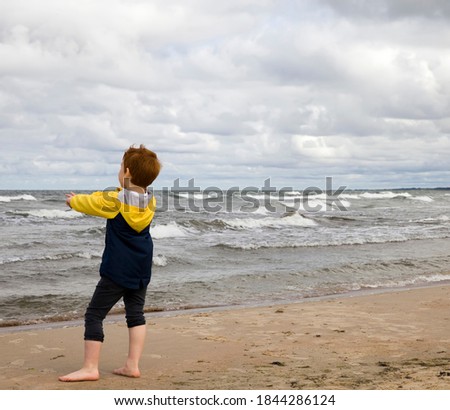 a boy in a yellow and black jacket walks along the Baltic sea coast, beautiful nature and a child during a holiday on the cold sea coast, sky