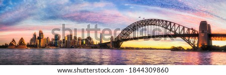 Colourful sunset in Sydney city across Harbour with major CBD landmarks - wide panorama.
