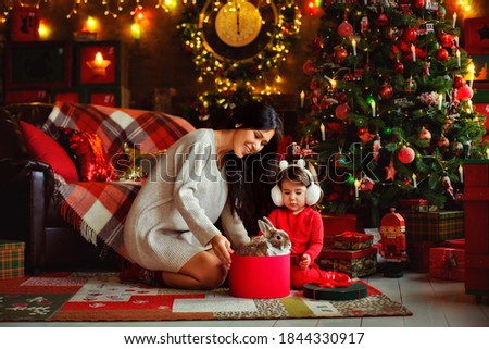 Mother and daughter celebrate Christmas. Family at the Christmas tree. A woman and a girl celebrate the New year with a rabbit
