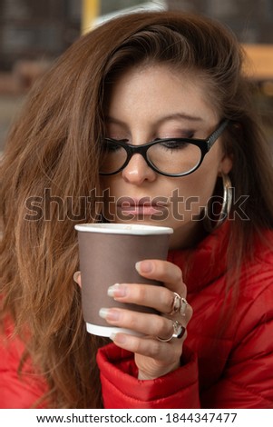face of young and beautiful latin woman, having a cup of coffee, uses makeup, glasses and red sweater, photo in the day