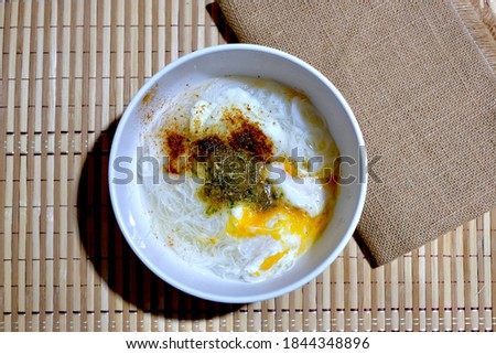 Noodles put eggs in a white cup on a brown wooden table.