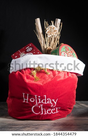 Santa Claus red bag with presents and gift showing Holiday Cheer. Isolated on black background.