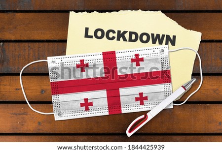 Flag of Georgia on Medical protective Surgical mask and word lockdown on paper. Coronavirus lockdown concept