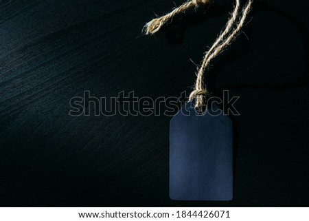 Concept of Black Friday. Empty label on a rope with space for text on black wooden background in sunlight.