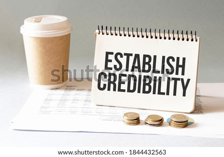 Hand with red pen. Cofee cup. Stick. Keyboard and white background. ESTABLISH CREDIBILITY sign in the notepad