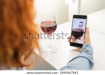 The women talk over video communication on the phone and drink red wine. The quarantined girl is not making a video call