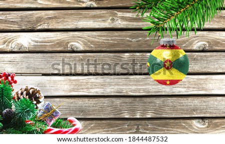 Concept of New Year and Christmas, on a wooden background, Christmas tree branches and a Christmas toy with the flag of Grenada.