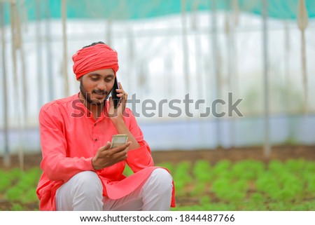 Young indian farmer using smartphone at greenhouse