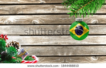 Concept of New Year and Christmas, on a wooden background, Christmas tree branches and a Christmas toy with the flag of Brazil.