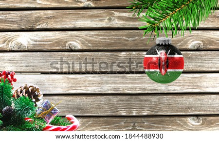 Concept of New Year and Christmas, on a wooden background, Christmas tree branches and a Christmas toy with the flag of Kenya.