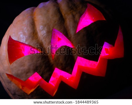 Halloween pumpkin with red eyes, scary face and spider on the eye, illuminated from inside with multicolored lights, very scary pumpkin for Halloween