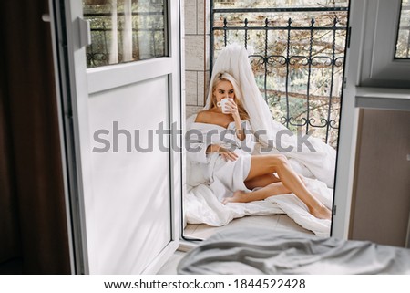 Young woman with a cup of coffee, wearing a bathrobe, at the balcony.