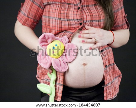 Pregnant woman holding a toy flower with black background