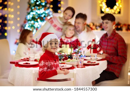 Family with children eating turkey Christmas dinner at fireplace and decorated Xmas tree. Parents, grandparents and kids at festive meal. Winter holidays celebration and food. Kids open presents.