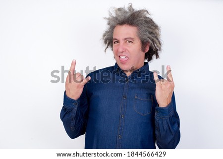 Handsome mature caucasian man with afro grey hair standing over isolated white background making rock hand gesture and showing tongue