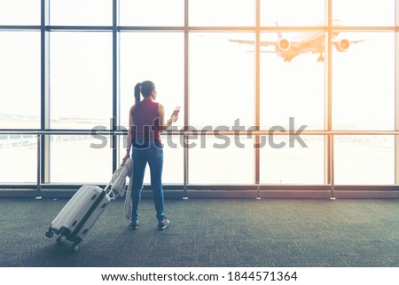 Traveler woman plan and backpack see airplane flight at the airport glass window, girl tourist happy hold bag and waiting luggage in hall airplane departure. Business people trip and Travel Concept
