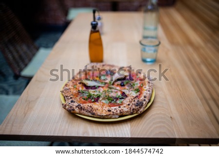Picture of a tasty looking vegan pizza on a wooden table alongside a bottle of salad dressing and a blurry glass of mineral water