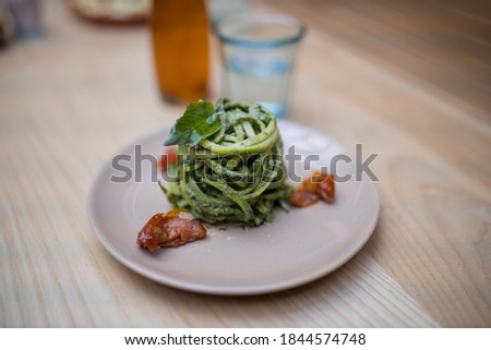 Close up picture of zucchini noodles with a spinach leaf on top on a wooden restaurant table and alongside a blurry glass of water and a bottle of salad dressing