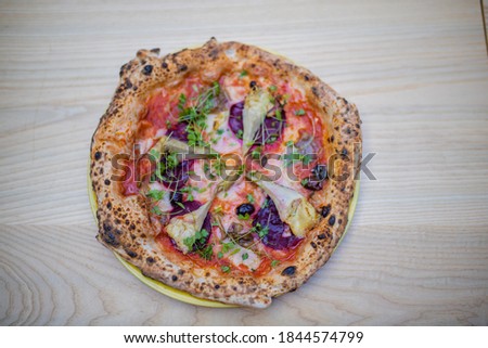 Above view of a thick and tasty looking full vegan pizza of several vegetarian ingredients, on a wooden table