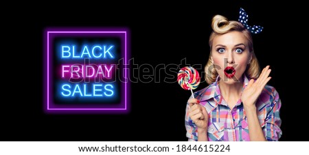 Excited surprised pinup woman with lollipop. Girl pin up with open mouth. Blond model at retro fashion and vintage concept. Dark background. Black Friday sales neon light sign. 