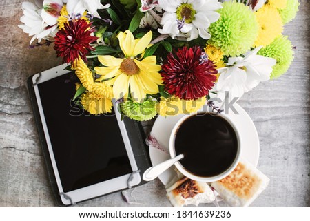 On the wooden table is a bouquet of flowers and chrysanthemums next to which is a tablet and a Cup of coffee with homemade cakes.
