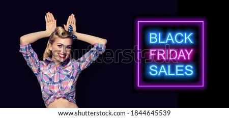 Pin up girl - funny bunny! Excited happy pinup woman holding hands on head in rabbit ears gesture. Retro fashion vintage concept. Dark background. Black Friday sales neon light sign. 
