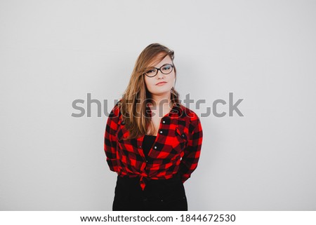 girl in a checkered red shirt and glasses on a background of white wall