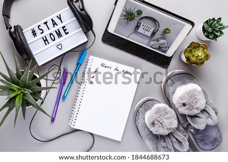 Light box in headphones with text STAY HOME, tablet, slippers and notepad on grey background. Healthcare and medical concept. Coronavirus, Quarantine and isolation concept. Covid-19, 2019-nCoV.