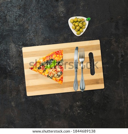 Top view of a pizza and olives. Stock photo of a pizza with a fork and a knife. American food. Composition of fast food on a dark background with copy space.