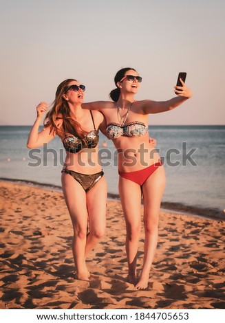 Mother and daughter make selfie on beach smiling and making funny faces. Mother and daugher teen brunettes are taking pictures with mobile phones on the beach.