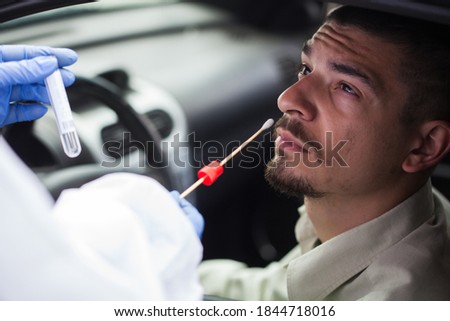 Medical UK worker performing drive-thru COVID-19 test,taking nasal swab specimen sample from male patient through car window,PCR diagnostic for Coronavirus presence,doctor in PPE holding test kit