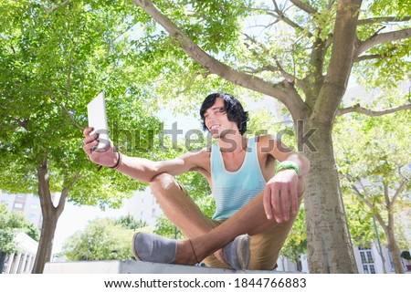Smiling young man clicking a picture using a digital tablet while sitting in a park