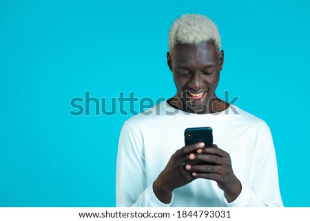 Handsome african man using smartphone on blue studio wall. Using modern technology - apps, social networks.
