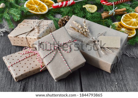 A bunch of Christmas boxes are lying on a wooden table. Green branches and oranges on the background