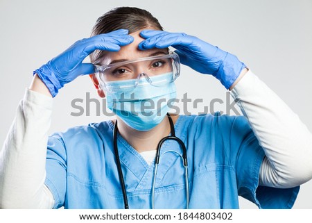 Desperate NHS UK medical EMS worker in white protective suit, head in hands,wearing blue surgical mask, latex gloves and safety goggles,Coronavirus COVID-19 pandemic crisis due to new Omicron variant