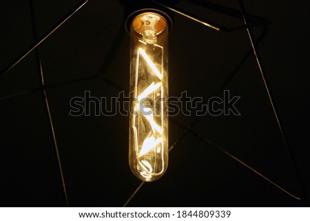 Close up image of a vintage filament light bulb glowing in the dark with detail of fingerprints on it