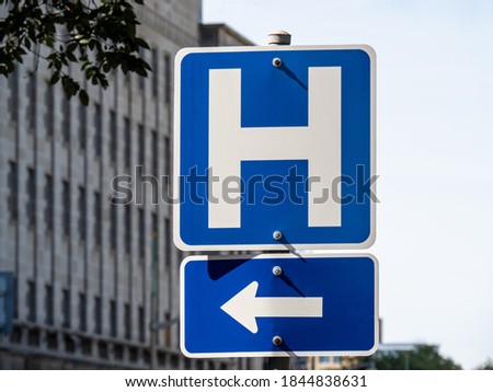 A blue hospital H sign with an arrow pointing left