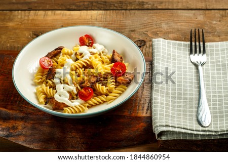 Pasta with chicken and cheese in a gray plate on a napkin with a fork.