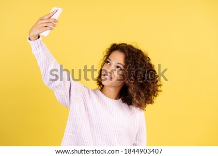 Smiling adult afro american woman social influencer making online stream in blog, using smartphone and standing on yellow copy space background
