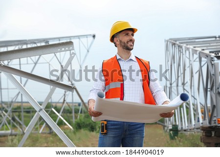 Professional engineer with plan near high voltage tower construction outdoors. Installation of electrical substation