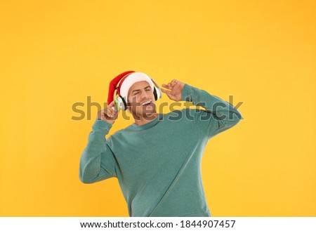Happy man with headphones on yellow background. Christmas music