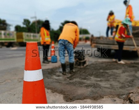 A blur of road maintenance work and an orange cone in the front.