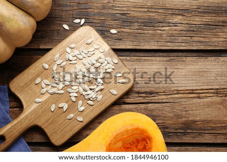 Raw seeds and fresh pumpkins on wooden table, flat lay. Space for text