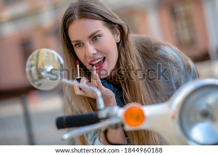 Stylish rider. A woman looking at a rear-view mirror while applying a lipstick