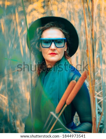 Stylish fashion woman in a green vintage dress, hat and glasses dancing among the autumn swamp with reeds.