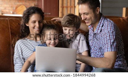 Wide banner panoramic view of smiling young family with two little kids look at laptop screen watch cartoon together. Happy parents with small children have fun talk speak on video call on computer.