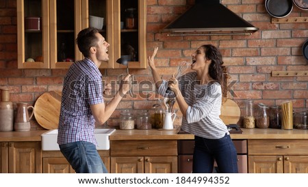 Wide panoramic view of overjoyed young Caucasian couple have fun on weekend in new home kitchen. Happy millennial man and woman renters dance and sing, entertain in own shared house together.