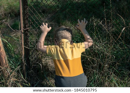 A little boy climbs into a hole in the fence